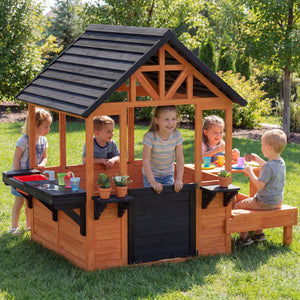 Maisonnette en bois pour enfants de 3 à 8 ans, avec table, bancs, évier, fenêtres et supports pour pots de fleurs, couleur marron.